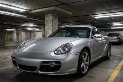 Porsche Cayman grise garée dans un parking urbain, vue trois-quarts avant sur fond de piliers en béton